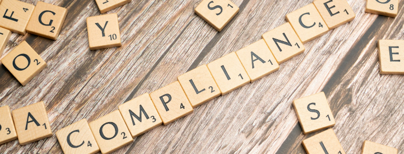 The word compliance spelled out with wooden letter tiles on a rustic table